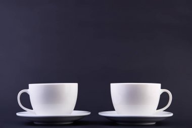 İki beyaz porselen çay bardaklarından koyu arka plan üzerinde izole temiz ve basit bir tasarım fikirleri göster.