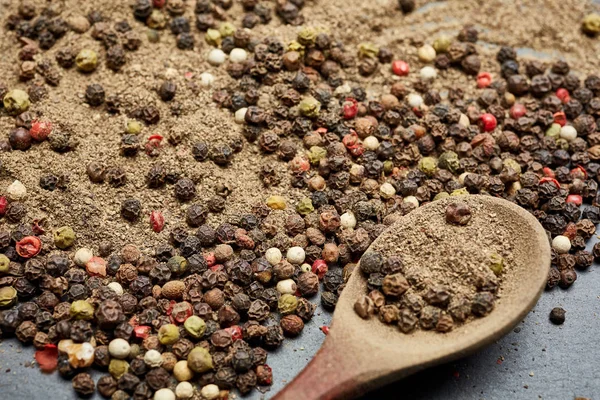 Cuchara de madera llena de semillas de pimienta de Jamaica y moler pimienta negra en la mezcla de fondo de pimientos, poca profundidad de campo — Foto de Stock