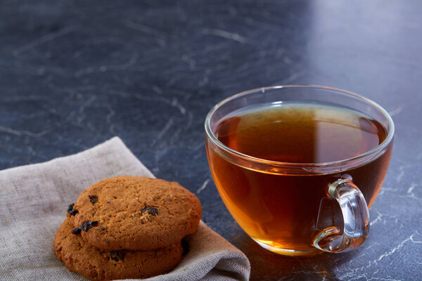 Shallow depth of field photo of a glass cup of black tea with brownies on a dark greyish marble background.