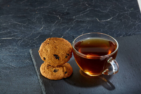 A glass cup of black tea with brownies on a dark greyish marble background. Breakfast background