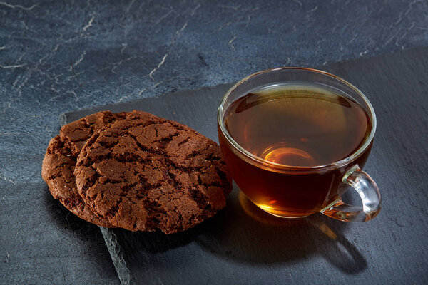 A glass cup of black tea with cookies on a dark greyish marble background. Breakfast background