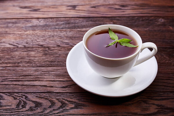 Фарфор белый китайский чашка черного чая и блюдце с мятой на винтажном фоне стола
.