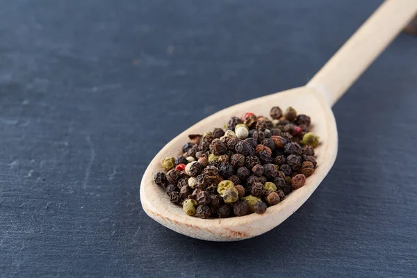 Top view of a wooden spoon full of allspice seeds isolated on dark background, shallow depth of field, front focus — Stock Photo, Image