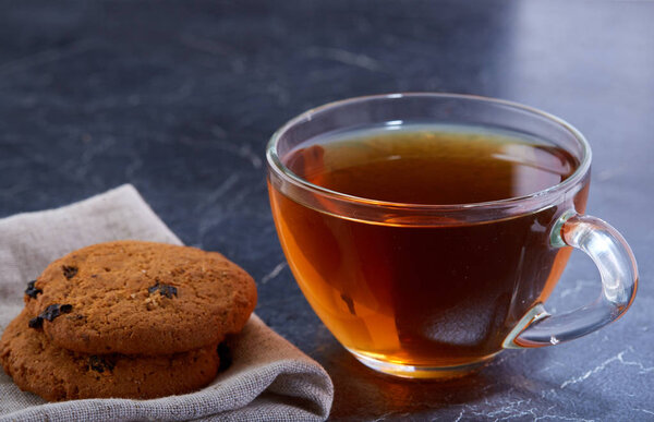 Shallow depth of field photo of a glass cup of black tea with brownies on a dark greyish marble background.