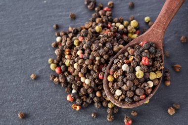 Siyah gıda arka plan baharatlar ile. Biber bir şeyl taş üzerinde bir tahta kaşıkla karışımı.