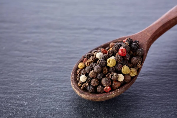 Zwarte peper erwten in een lepel op een steen — Stockfoto