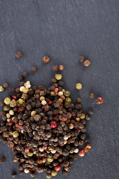 bulk of various pepper peppercorns seeds mix on dark stone
