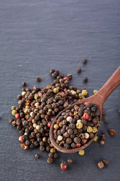 Fundo de comida preta com especiarias. Uma mistura de pimentas com uma colher de madeira em uma pedra de xisto . — Fotografia de Stock