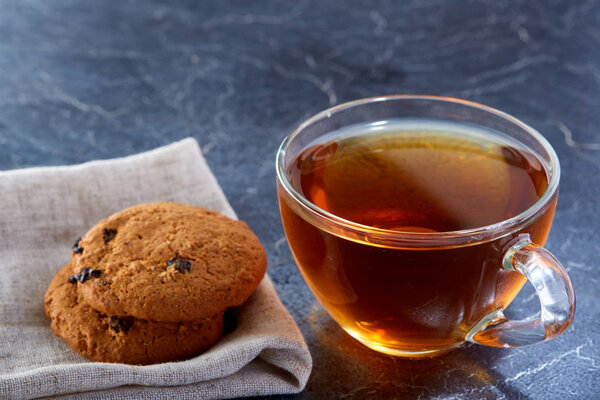 Shallow depth of field photo of a glass cup of black tea with brownies on a dark greyish marble background.