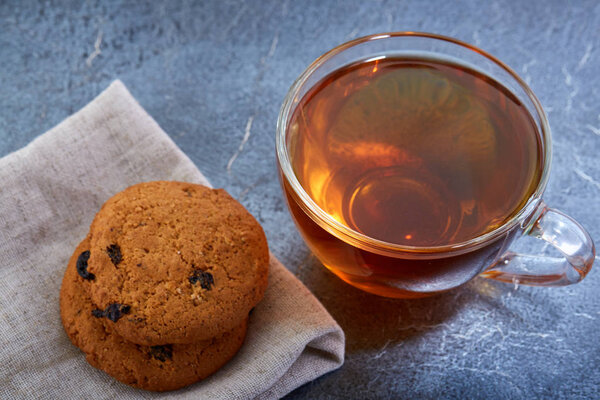A glass cup of black tea with cookies on a dark greyish marble background, shallow depth of field. Breakfast background