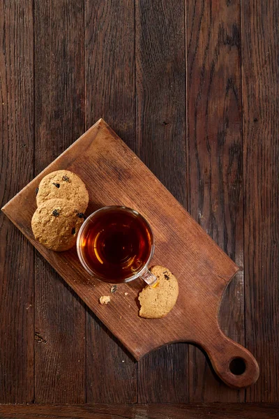 Taza de té con galletas en una tabla de cortar sobre un fondo de madera, vista superior, vertical — Foto de Stock