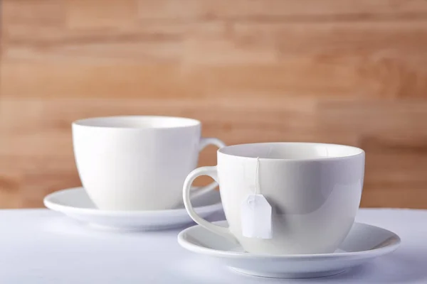 Two cups of tea and a teabag on white table on rustic wooden background, close-up, selective focus