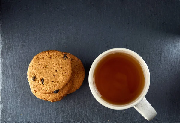 Primer plano taza blanca de té con galletas de chocolate sobre fondo oscuro, vista superior — Foto de Stock