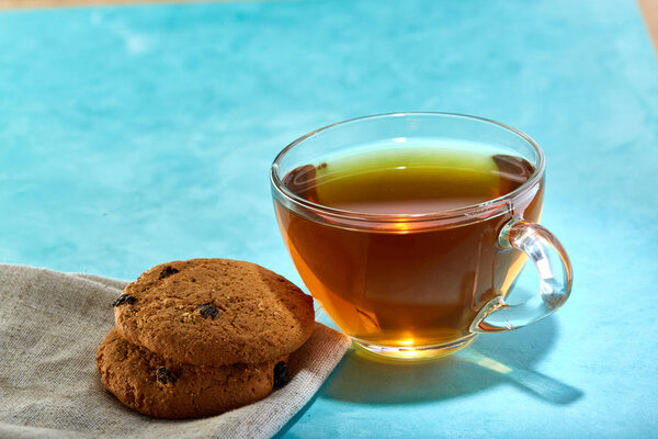 Glass cup of tea and chocolate cookies close-up on blue background.