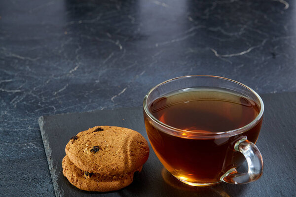 A glass cup of black tea with cookies on a dark greyish marble background. Breakfast background