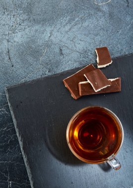 Cam bardak koyu grimsi mermer zemin üzerine çikolata parçaları ile siyah çay. Üstten Görünüm