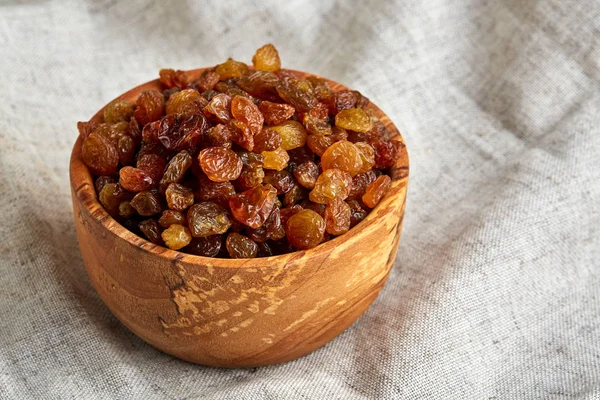 Wooden bowl with golden raisins on light tablecloth, close-up, selective focus — Stock Photo, Image