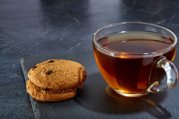 Shallow depth of field photo of a glass cup of black tea with brownies on a dark greyish marble background.