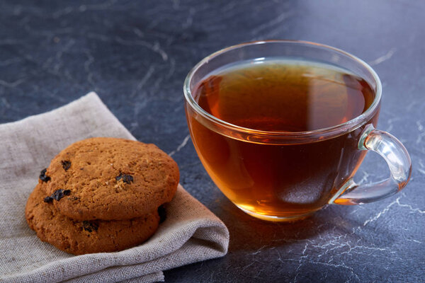 A glass cup of black tea with cookies on a dark greyish marble background. Breakfast background
