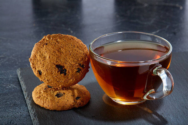 A glass cup of black tea with cookies on a dark greyish marble background. Breakfast background
