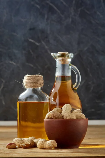 Óleo aromático em frasco de vidro e garrafa com amendoim em tigela sobre mesa de madeira, close-up, vertical — Fotografia de Stock