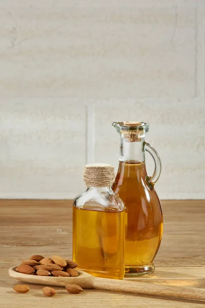 Óleo aromático em um jarro de vidro e garrafa com amêndoa em uma colher na mesa de madeira, close-up . — Fotografia de Stock