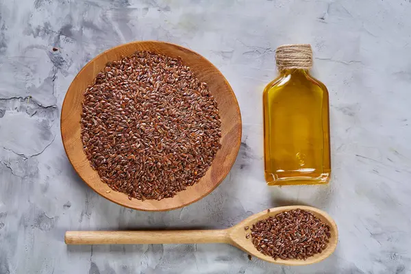 Semillas de lino en cuenco y aceite de linaza en botella de vidrio sobre fondo de madera, vista superior, primer plano, enfoque selectivo — Foto de Stock