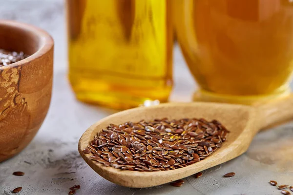 Semillas de lino en cuenco y aceite de linaza en botella de vidrio sobre fondo de madera, vista superior, primer plano, enfoque selectivo — Foto de Stock