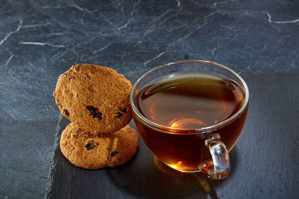 A glass cup of black tea with cookies on a dark greyish marble background. Breakfast background