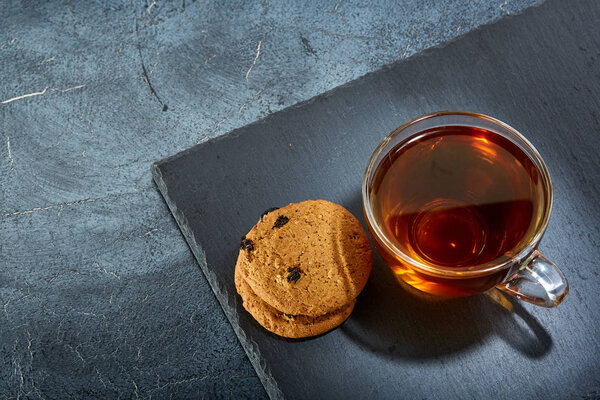 A glass cup of black tea with cookies on a dark greyish marble background. Breakfast background