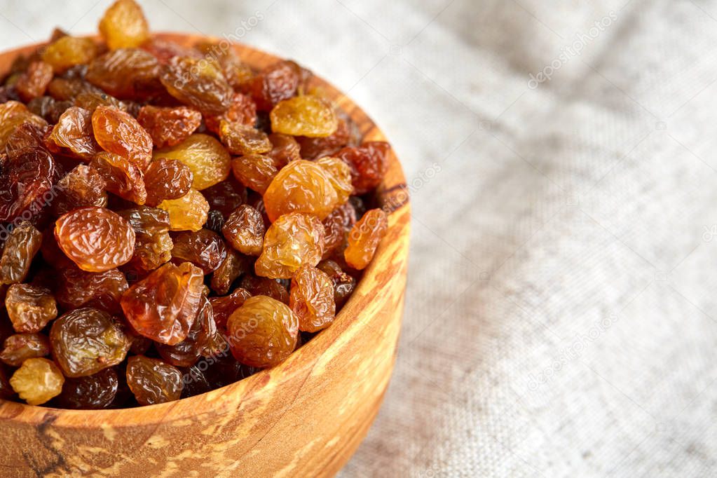 Wooden bowl with golden raisins on light tablecloth, close-up, selective focus