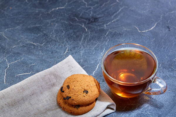 A glass cup of black tea with cookies on a dark greyish marble background, shallow depth of field. Breakfast background