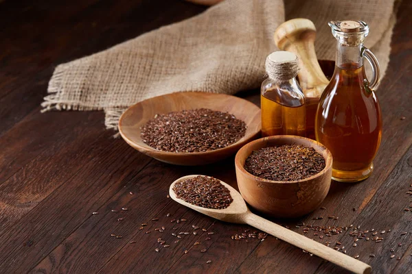 Semillas de lino en cuenco y aceite de linaza en botella de vidrio sobre fondo de madera, vista superior, primer plano, enfoque selectivo — Foto de Stock