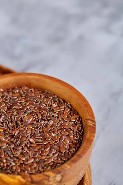 Flax seeds in bowl and flaxseed oil in glass bottle on light textured background, top view, close-up, selective focus