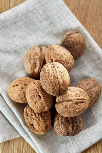 A stack of hard shells of walnuts piled together on light grey fabric cotton tablecloth, selective focus