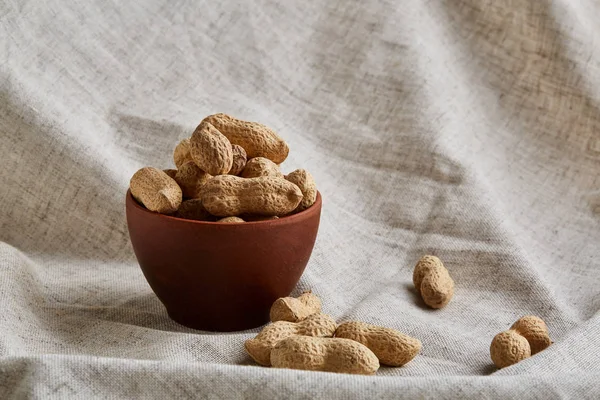 Unpeeled peanuts in ceramic bowl closeup, selective focus