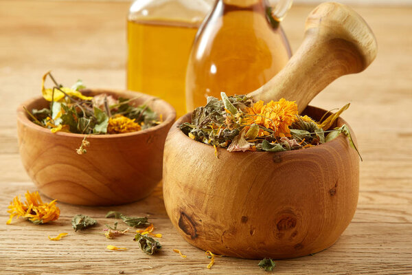 Picturesque composition of oil jars, pestle and mortar with motley grass over wooden background, selective focus.