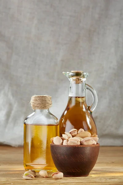 Óleo aromático em um frasco de vidro e garrafa com pistache em tigela na mesa de madeira, close-up — Fotografia de Stock