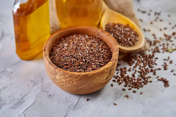 Semillas de lino en cuenco y aceite de linaza en botella de vidrio sobre fondo texturizado claro, vista superior, primer plano, enfoque selectivo — Foto de Stock