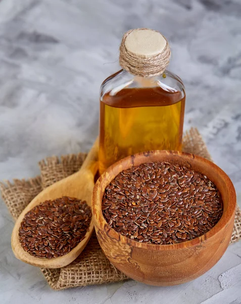 Semillas de lino en cuenco y aceite de linaza en botella de vidrio sobre fondo texturizado claro, vista superior, primer plano, enfoque selectivo — Foto de Stock