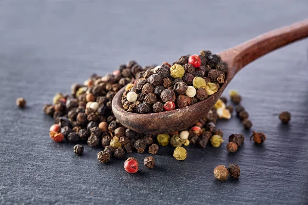 Vue de dessus sur la composition des grains de poivre dans une cuillère en bois sur fond sombre, gros plan . — Photo