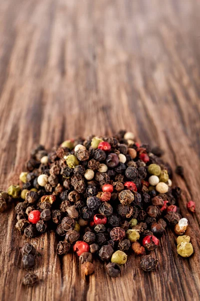 Draufsicht auf schwarze, rote und weiße Pfefferkörner isoliert auf Holzgrund, geringe Schärfentiefe. — Stockfoto