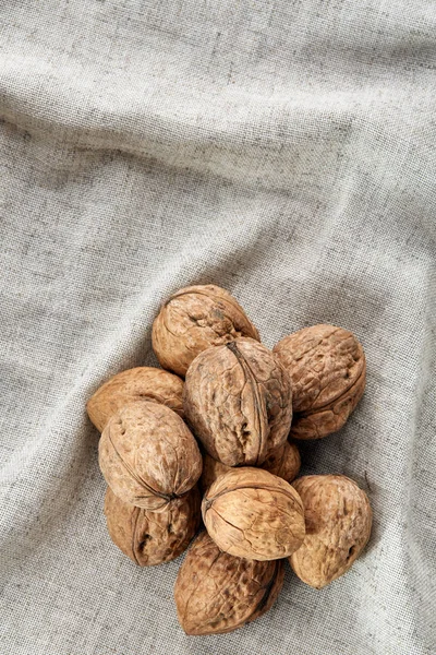 A stack of hard shells of walnuts piled together on light grey fabric cotton tablecloth, selective focus