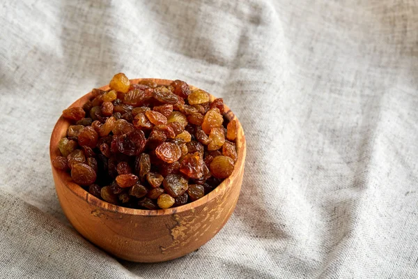 Wooden bowl with golden raisins on light tablecloth, close-up, selective focus — Stock Photo, Image