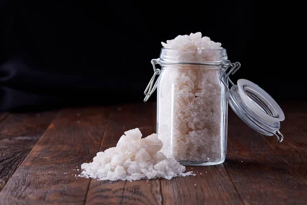 Spa concept. Bath salt pouring out of glass jar on wooden table, close-up, selective focus — Stock Photo, Image