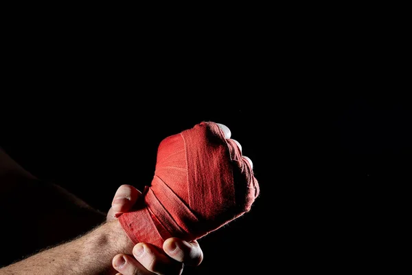 Uma bandagem vermelha boxers em sua mão isolado em fundo escuro desfocado, close-up . — Fotografia de Stock