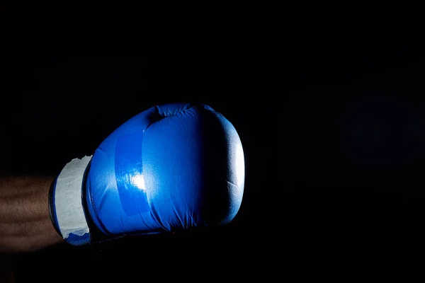 Een blauwe strijders bokshandschoenen op zijn hand geïsoleerd op donkere onscherpe achtergrond, close-up. — Stockfoto