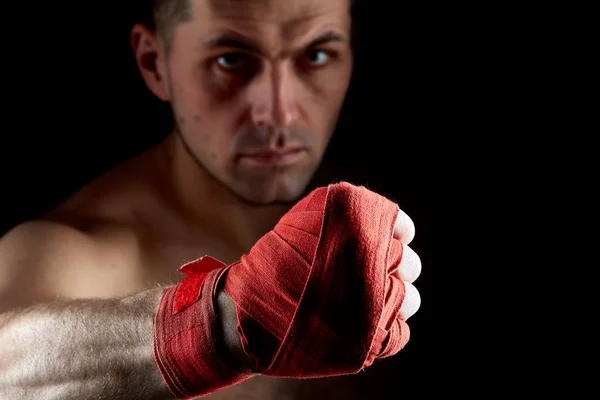 Close up low key portrait of an aggressive muscular fighter, showing his fist on dark background, selective focus — Stock Photo, Image