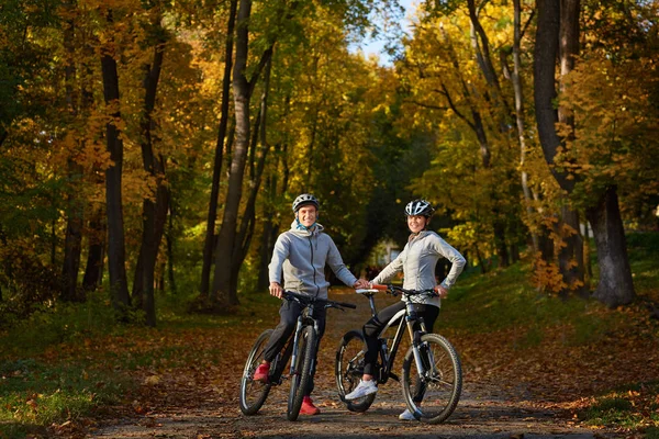 Felice giovane coppia che va a fare un giro in bicicletta in una giornata autunnale nel parco . — Foto Stock