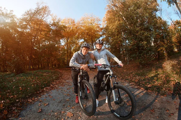 Felice giovane coppia che va a fare un giro in bicicletta in una giornata autunnale nel parco, retroilluminazione . — Foto Stock